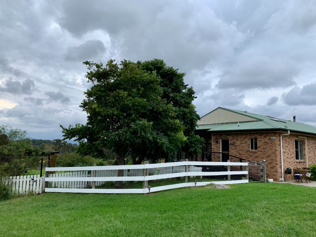 The brick farmstay house behind a white fence, with hills in the distance